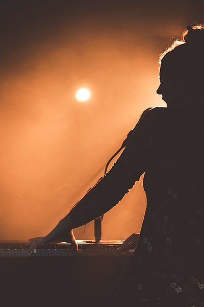 A silhouette of a woman playing a keyboard in front of a light.