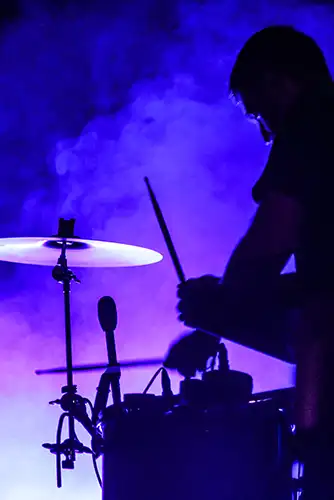 A drummer performing in front of a purple haze.