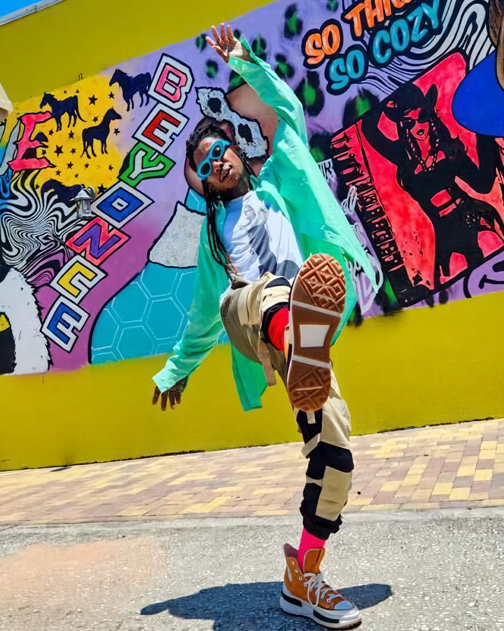 A young man dancing in front of a colorful wall.