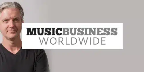 A person with gray hair stands beside a logo reading "MUSIC BUSINESS WORLDWIDE" against a plain background, as if prepared for a press event.