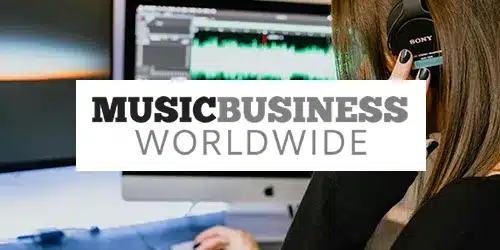 Person listening to headphones in front of a computer screen with audio editing software, overlaid text reads "Music Business Worldwide Press.