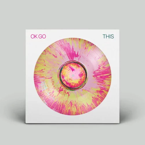 A vinyl record with a pink and yellow splatter pattern highlights the artistry of physical music distribution, displayed in a white sleeve labeled "OK GO" in pink and "THIS" in green.