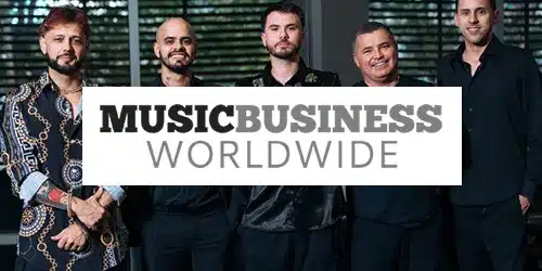 Five men stand together indoors, dressed in black, as blinds cover the windows behind them. Overlaid text reads "Music Business Worldwide," suggesting a press event or announcement.