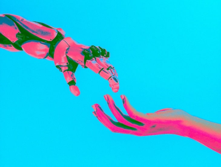 A robotic hand reaches toward a human hand against a bright blue background, illustrating interaction between technology and humanity.