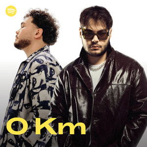 Two men pose against a white background; one faces sideways in a patterned shirt, the other faces forward in sunglasses and a black leather jacket. The Protoje Case Study text "O Km" appears in yellow.